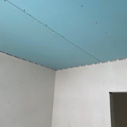 Konrad Sobol - Niebieska płyta gipsowo-kartonowa zamontowana na suficie, z widocznymi śladami po wkrętach i taśmą marki Sinat na styku ze ścianą, z elementami instalacji elektrycznej wystającymi z sufitu.