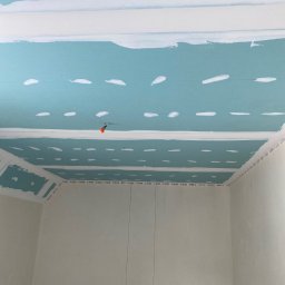 Konrad Sobol - Montaż sufitu podwieszanego z płyt kartonowo-gipsowych, widoczne szpachlowane łączenia i instalacja elektryczna wystająca z sufitu.