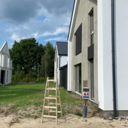 Budowa domu jednorodzinnego: surowy stan z ocieploną elewacją i drewnianą drabiną przyłączeniową