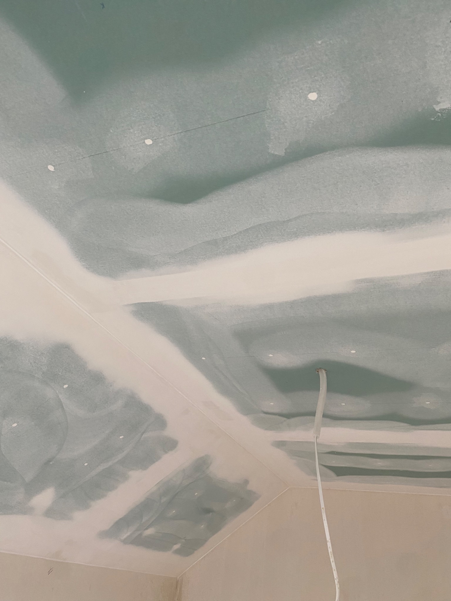 Niedokończony sufit z płyt kartonowo-gipsowych z widocznymi łączeniami i szpachlą, wystający przewód elektryczny.