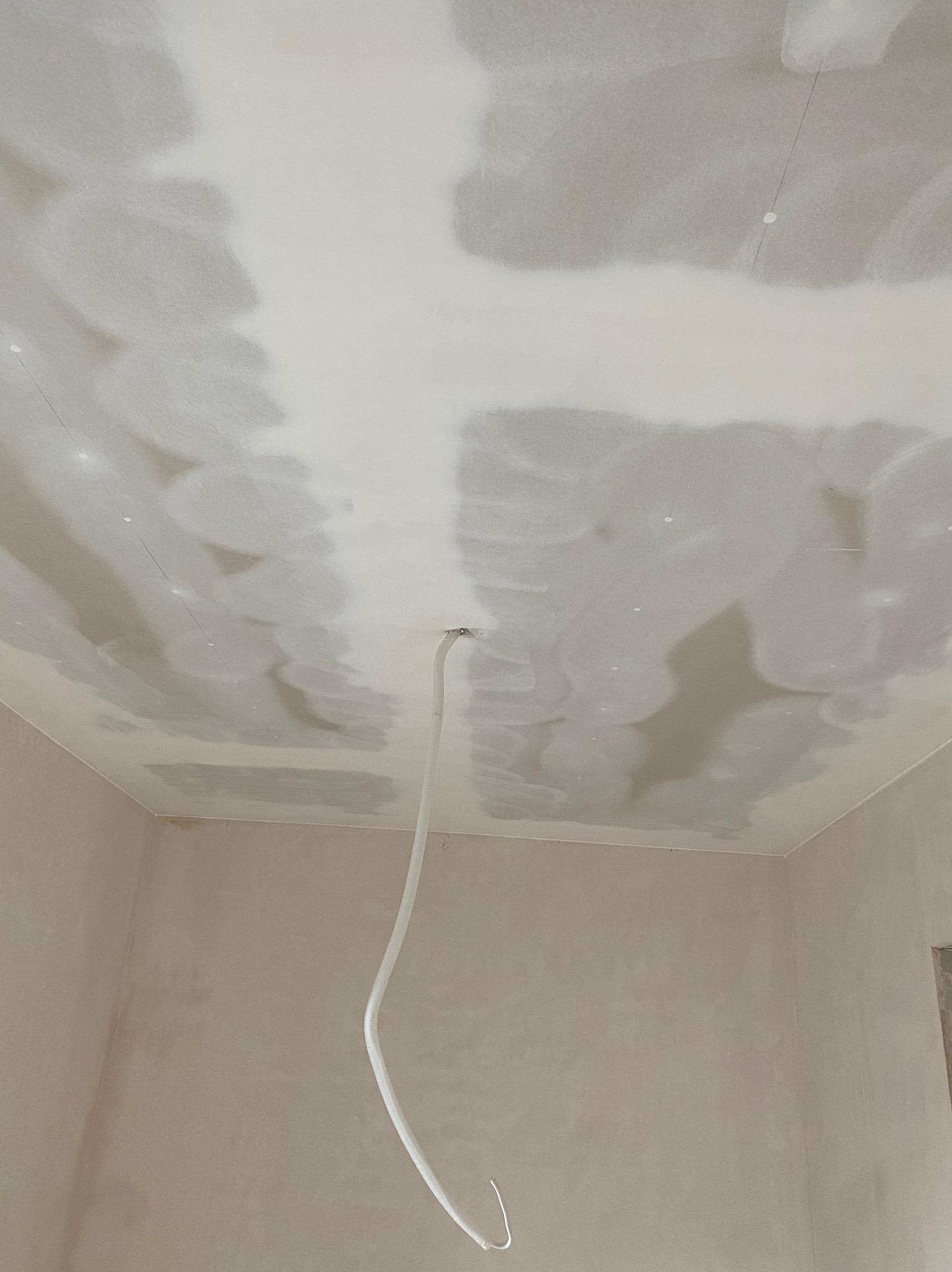 Szpachlowana powierzchnia sufitu z widocznym przewodem elektrycznym, przygotowana do dalszych prac wykończeniowych.