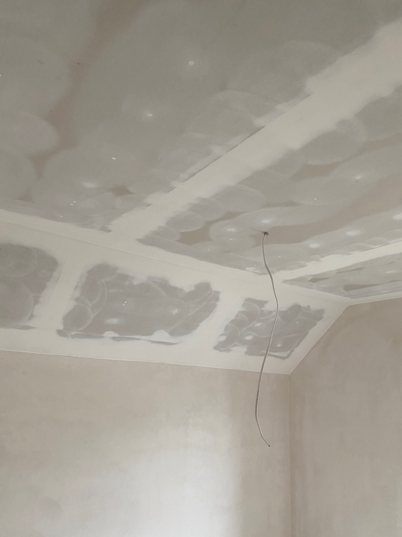 Sufit podwieszany z płyt gipsowo-kartonowych w trakcie szpachlowania, widoczny przewód elektryczny zwisający z otworu, niedokończone połączenia płyt.