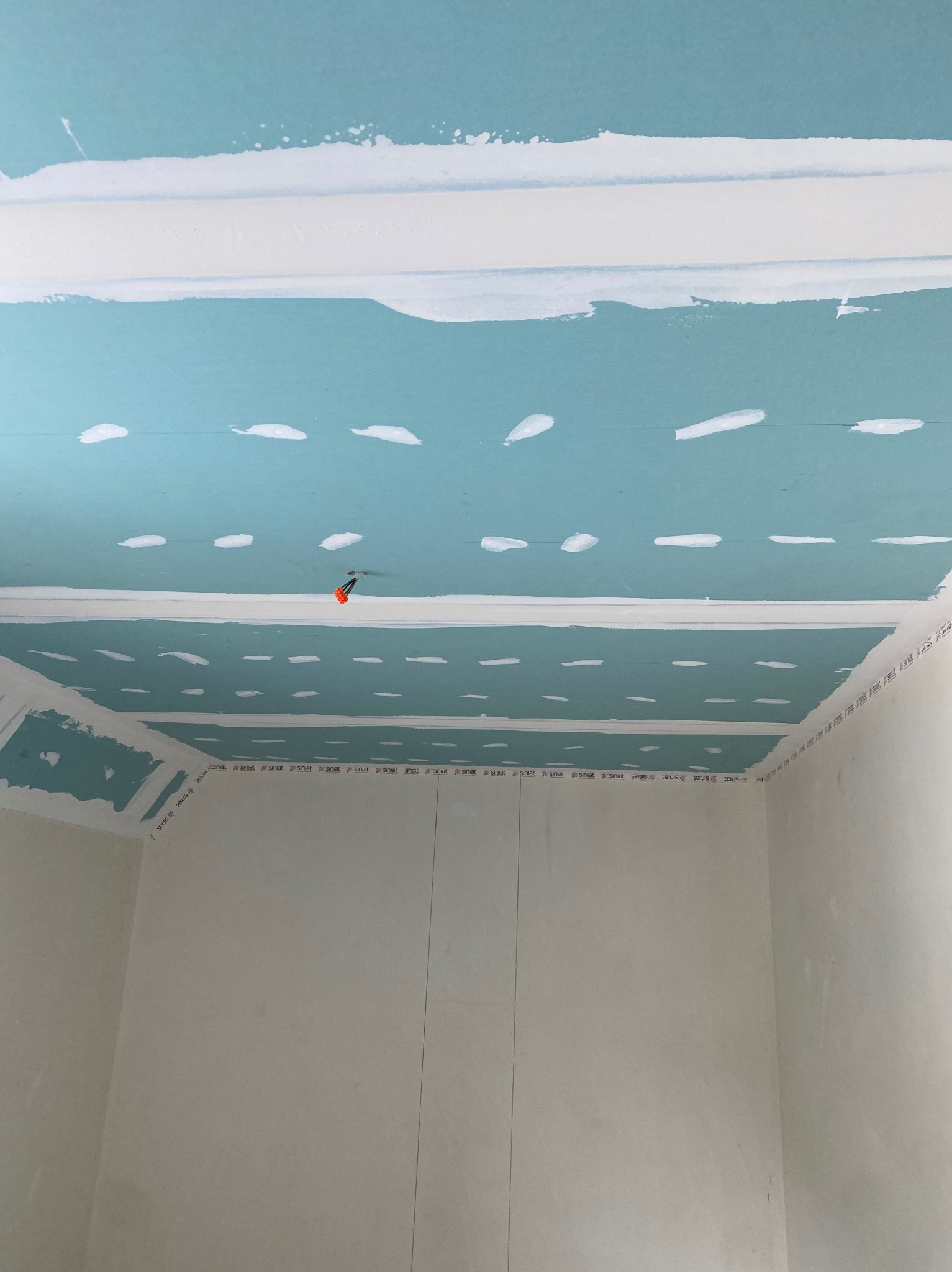 Montaż sufitu podwieszanego z płyt kartonowo-gipsowych, widoczne szpachlowane łączenia i instalacja elektryczna wystająca z sufitu.