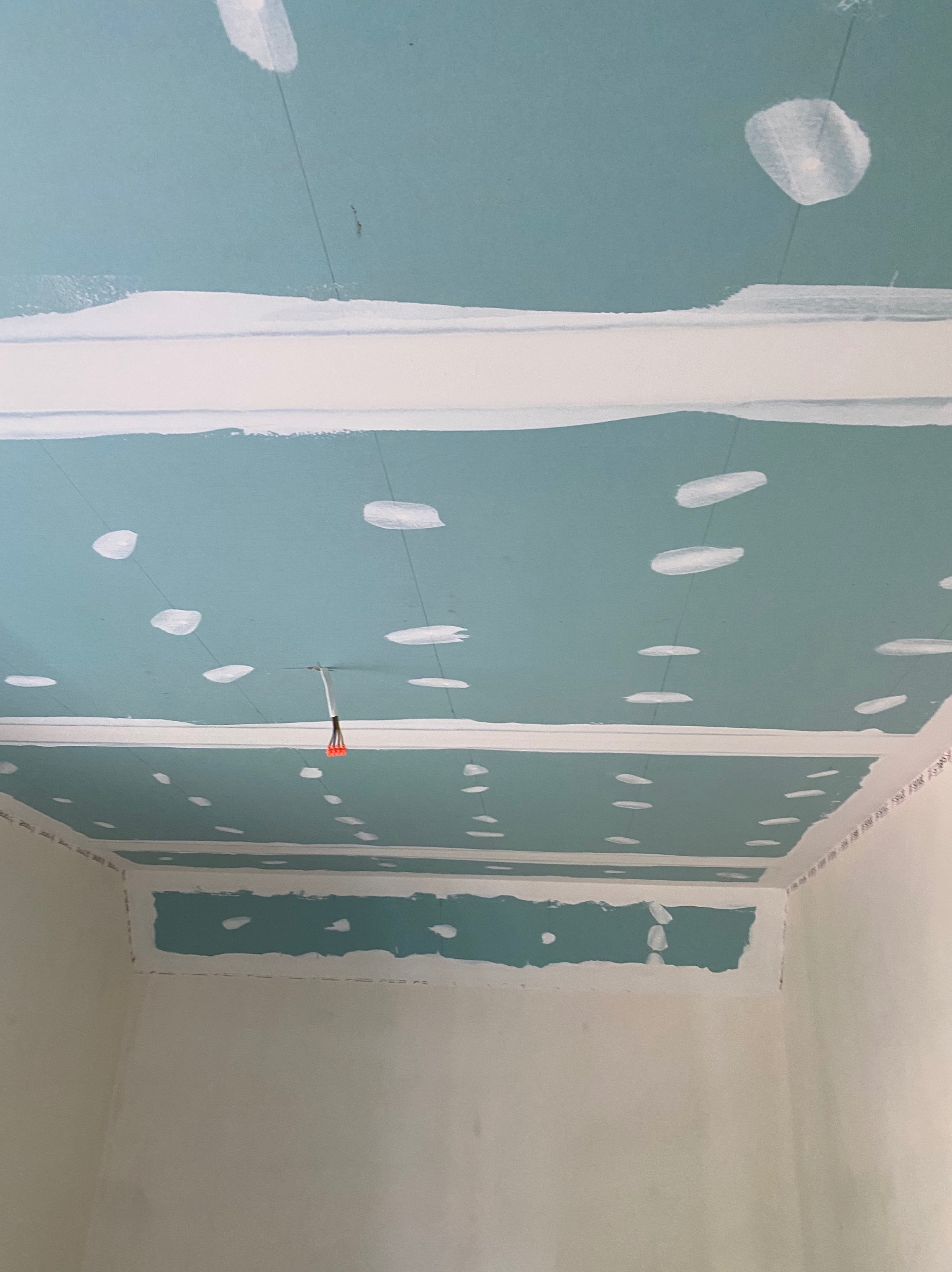 Niedokończony sufit z płyt gipsowo-kartonowych, widoczne łączenia szpachlowane, wystające kable elektryczne, ściany w stanie surowym.