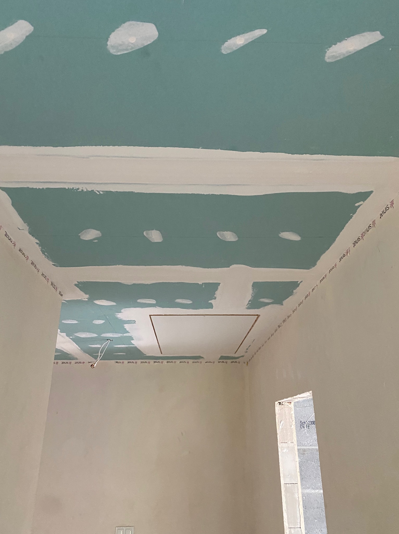 Niedokończony sufit podwieszany z płyty gipsowo-kartonowej, widoczne łączenia i szpachlowanie, listwy wykończeniowe z nadrukiem producenta, instalacja elektryczna wystająca z sufitu.