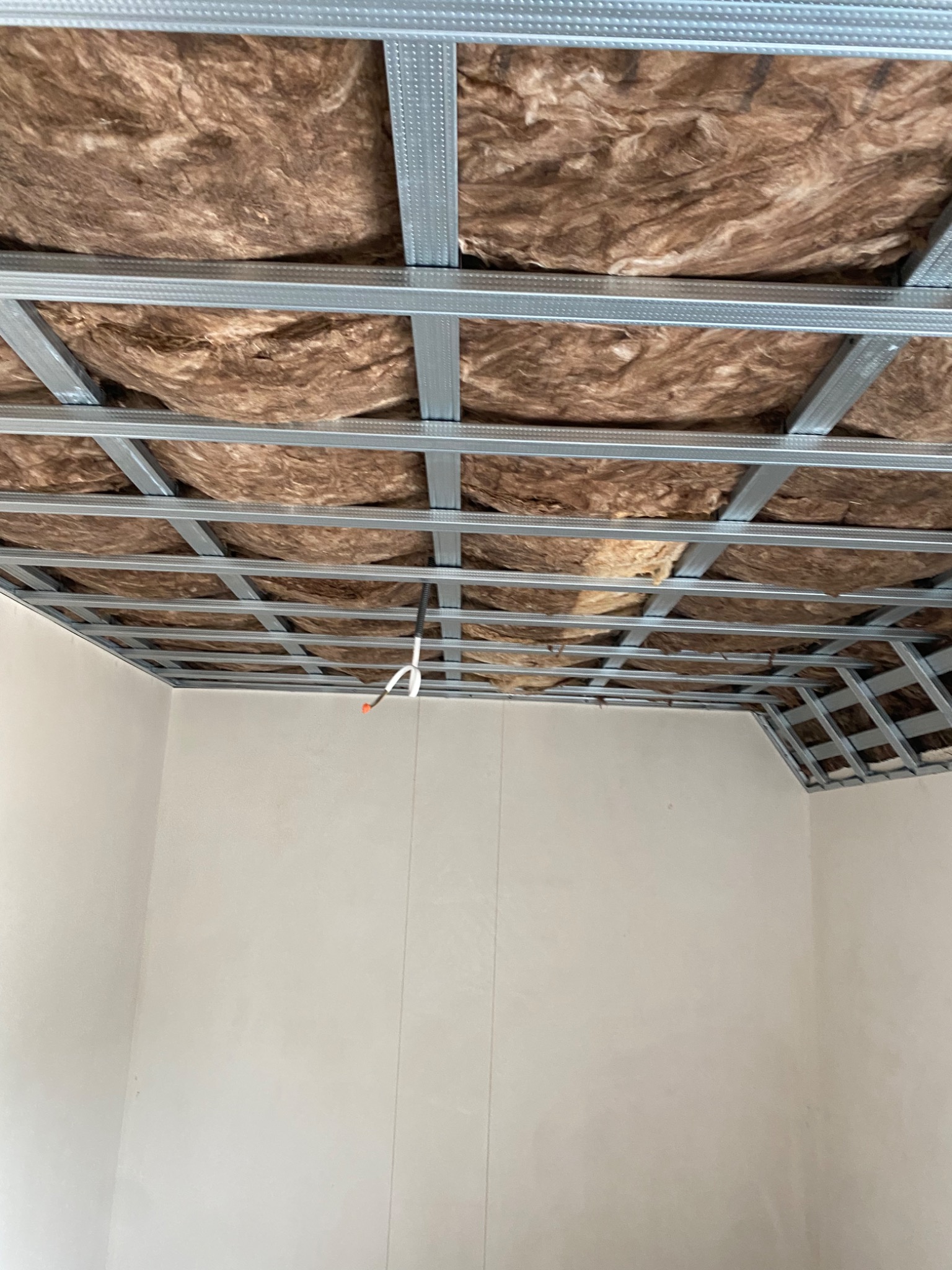 Sufit podwieszany z metalowym stelażem i wełną mineralną w trakcie montażu w Strachowie, widoczne przewody elektryczne.