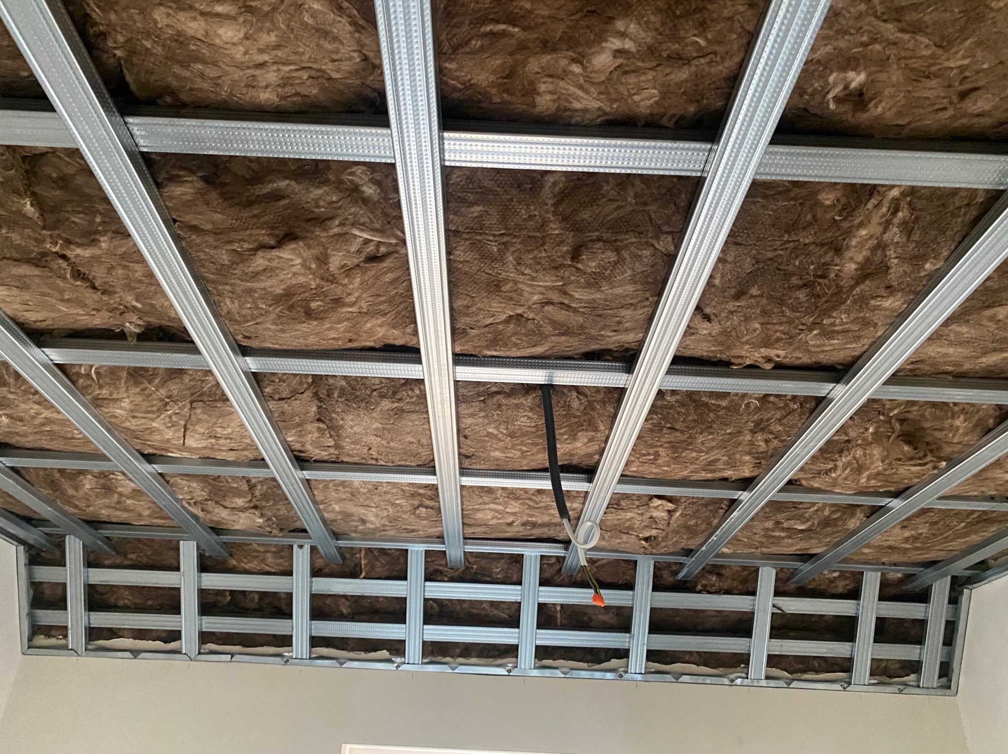 Montaż wełny mineralnej w metalowym ruszcie sufitu podwieszanego z płyty karton gips, widoczne przewody elektryczne