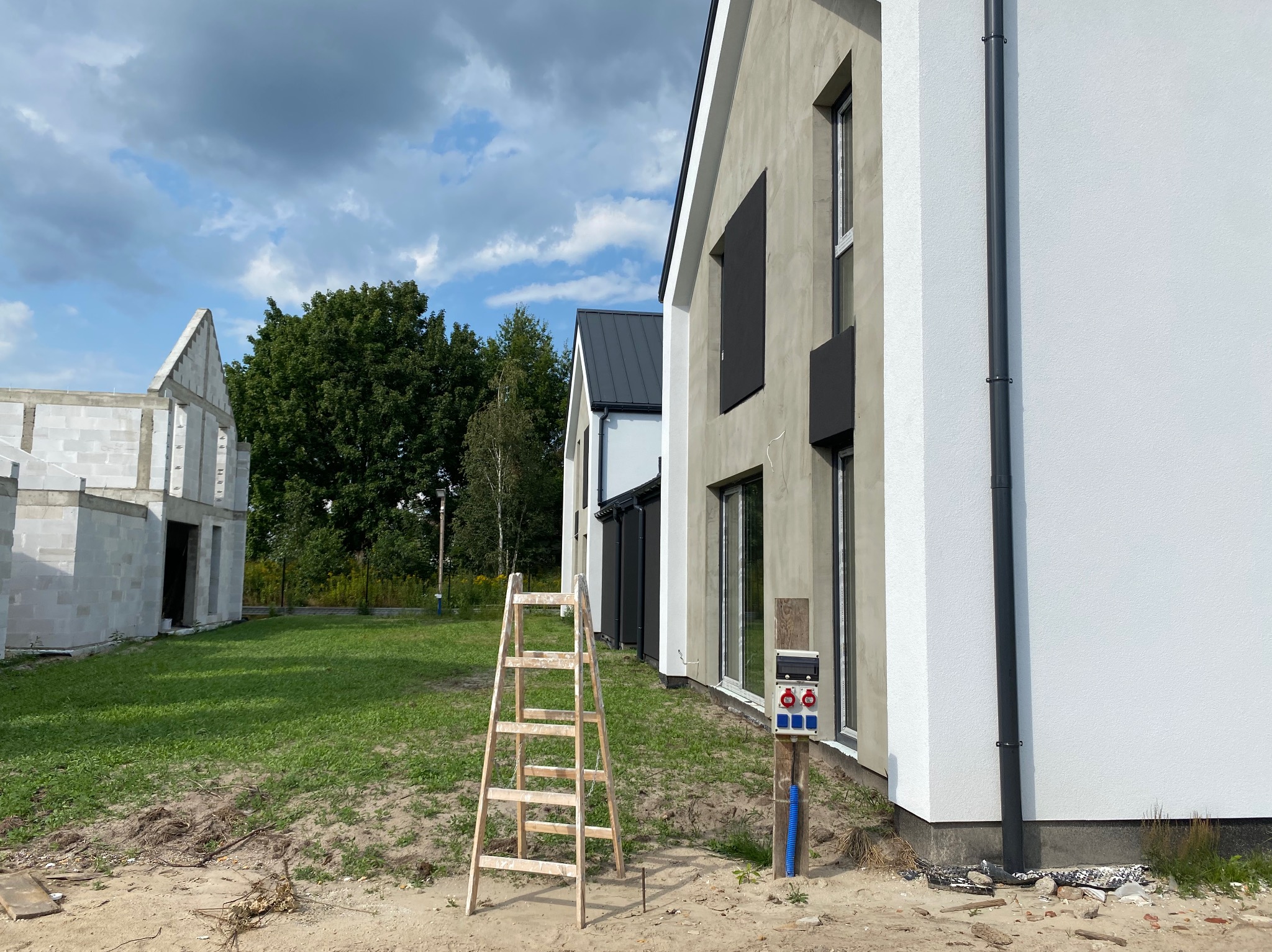 Budowa domu jednorodzinnego: surowy stan z ocieploną elewacją i drewnianą drabiną przyłączeniową