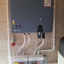 SUN ENERGY ŁUKASZ KACZMAREK - Szczegółowe ujęcie instalacji fotowoltaicznej w Luta, prezentujące falownik marki Solplanet, rozdzielnice PV DC i AC, oraz okablowanie na tle płytek imitujących drewno.