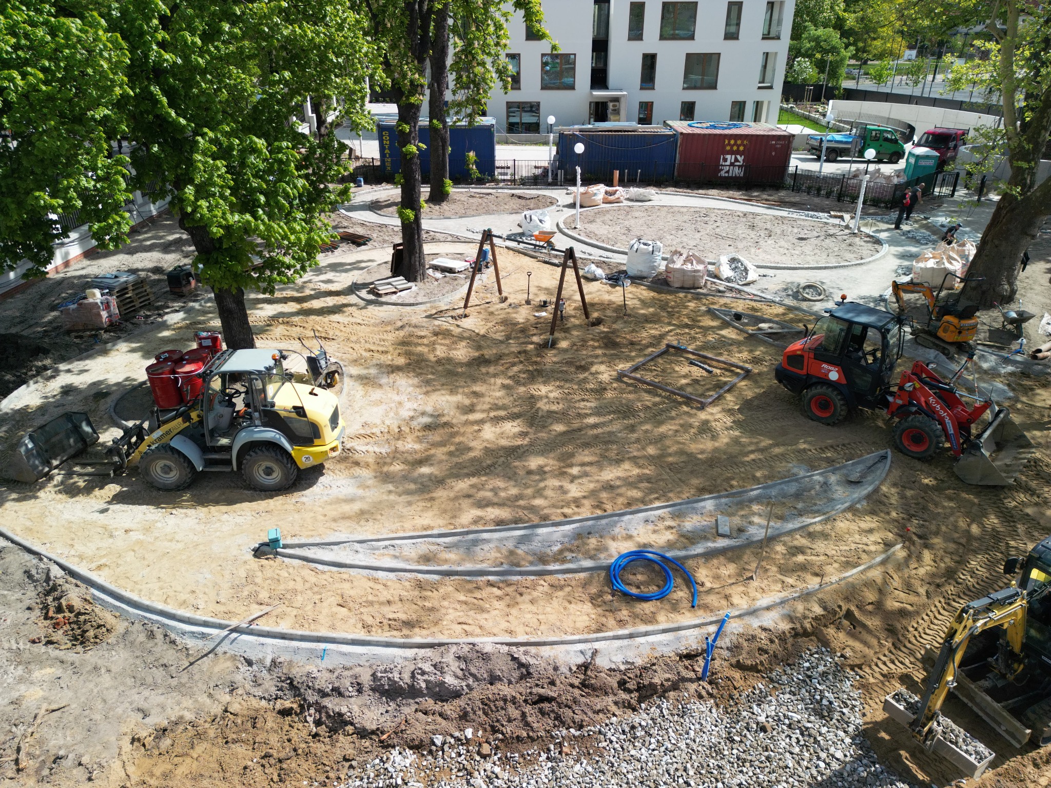 Plac budowy placu zabaw we Wrocławiu z kostką brukową w trakcie układania, widok z góry. Traktory, piasek i elementy placu zabaw.