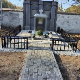Artystal Paweł Krzan - Czarne metalowe ogrodzenie otacza pomnik na cmentarzu, z wybrukowaną ścieżką prowadzącą do grobu.