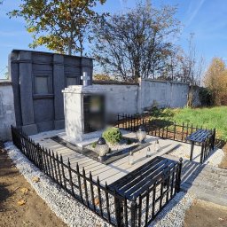 Artystal Paweł Krzan - Nagrobek z marmuru otoczony niskim, czarnym ogrodzeniem metalowym z dwoma ławkami, całość wysypana drobnymi, białymi kamieniami, w tle nagrobki i drzewa.