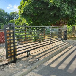 Artystal Paweł Krzan - Przesuwna brama wjazdowa z poziomymi profilami, zamontowana na betonowym fundamencie, widoczna od strony ulicy z cieniem rzucanym przez konstrukcję.