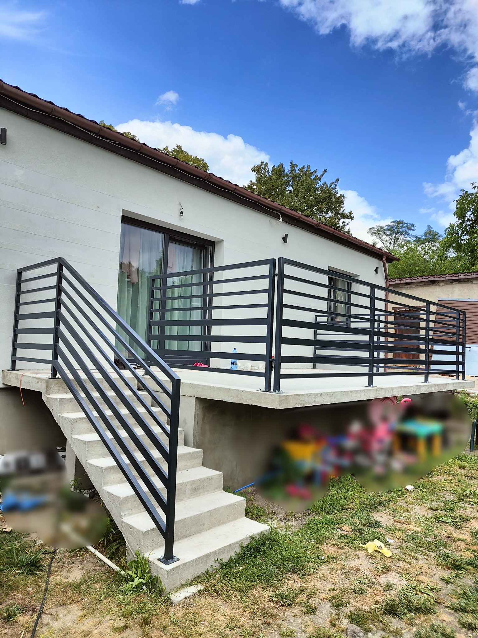 Nowoczesna, pozioma balustrada z czarnych profili na schodach i balkonie domu z białymi ścianami, widok z dołu na tle błękitnego nieba.