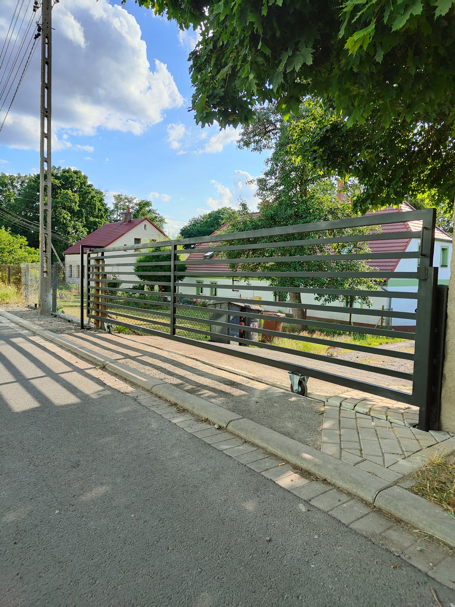 Przesuwna brama z poziomych profili, zamontowana na posesji w Pieńsku, widoczna na tle domu z czerwonym dachem i zieleni drzew.