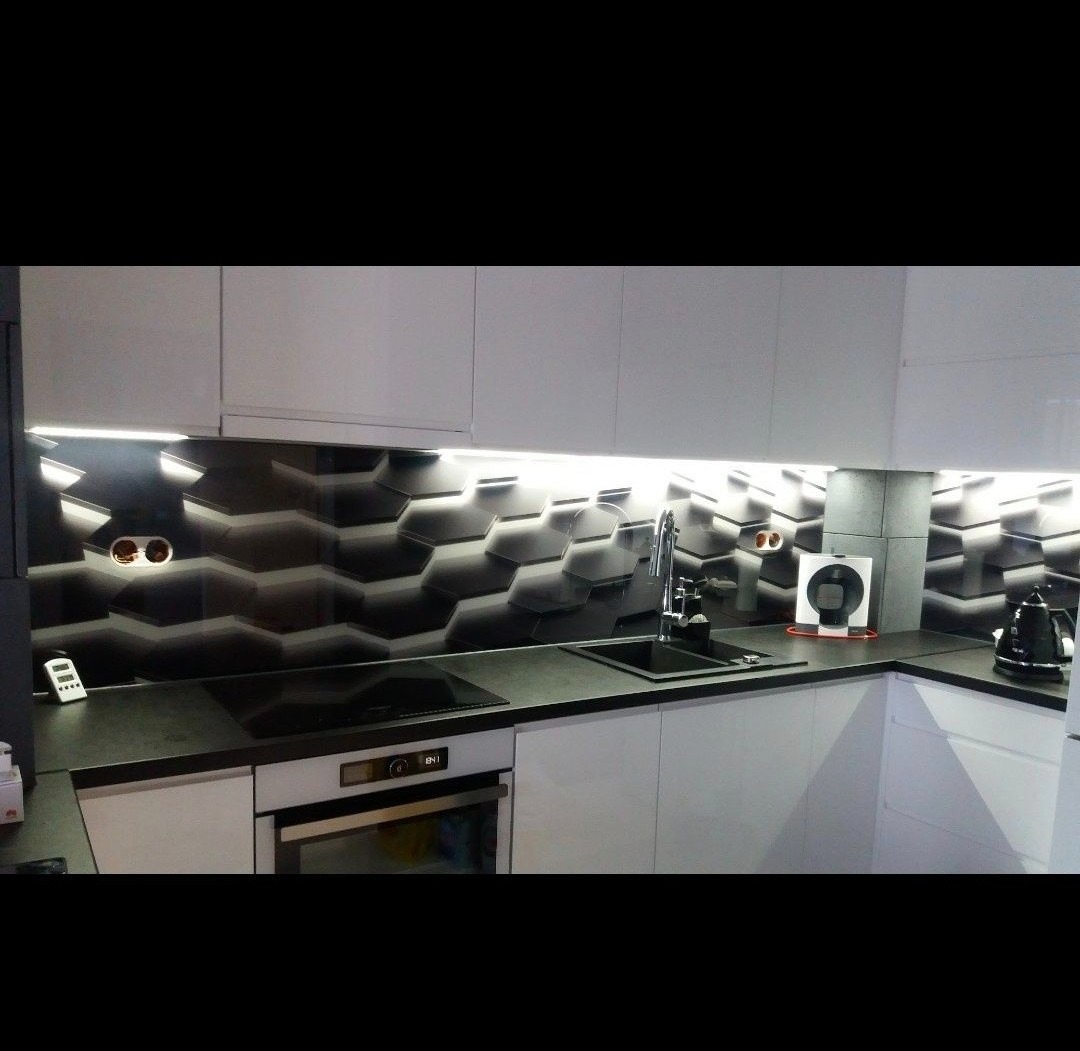 Nowoczesna kuchnia z czarno-białą szklaną ścianą w heksagonalne wzory podświetloną LED, jasne szafki i czarny blat.