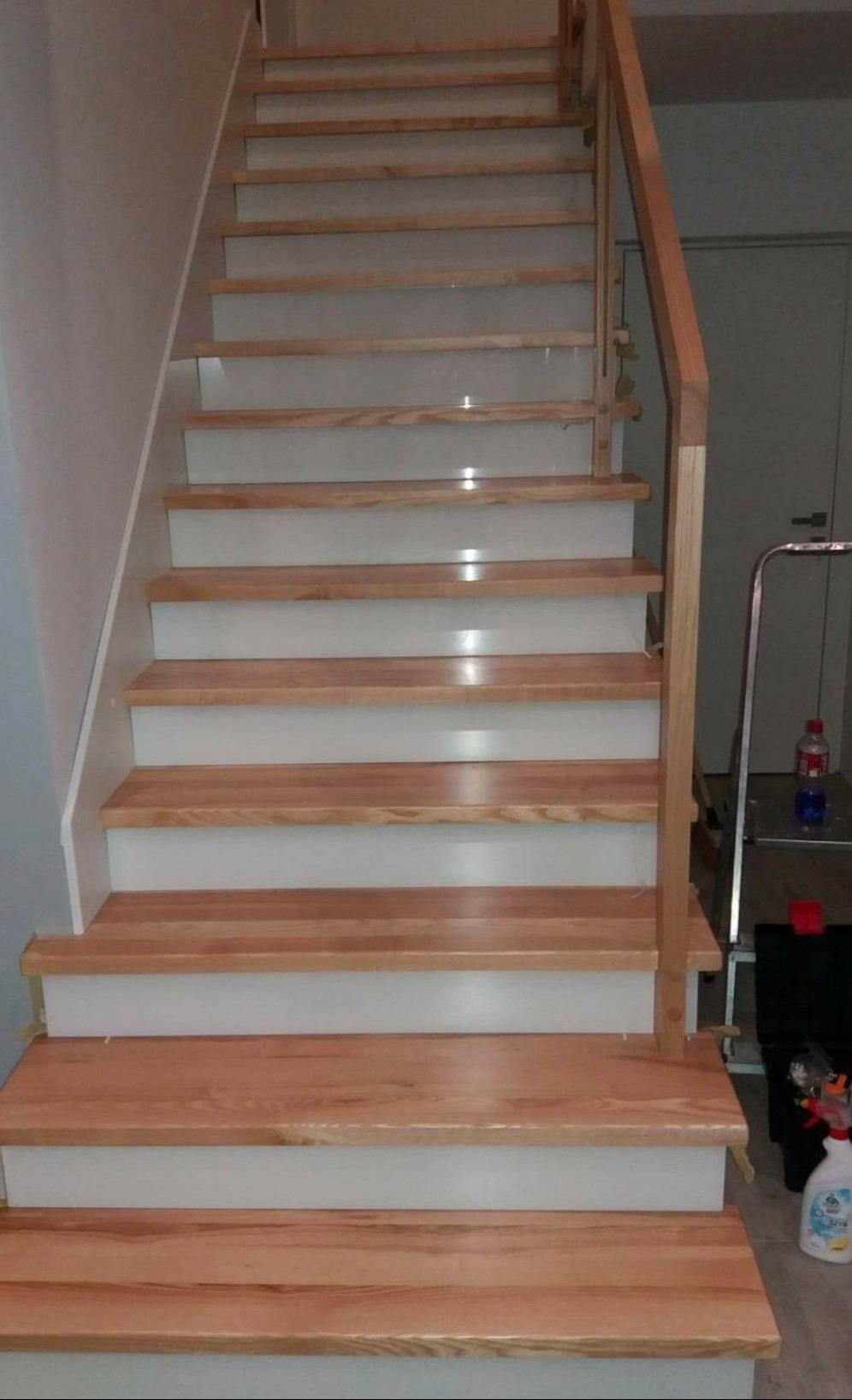 Schody drewniane z białymi podstopnicami i drewnianą balustradą, widoczne z dołu, z akcesoriami malarskimi w tle.