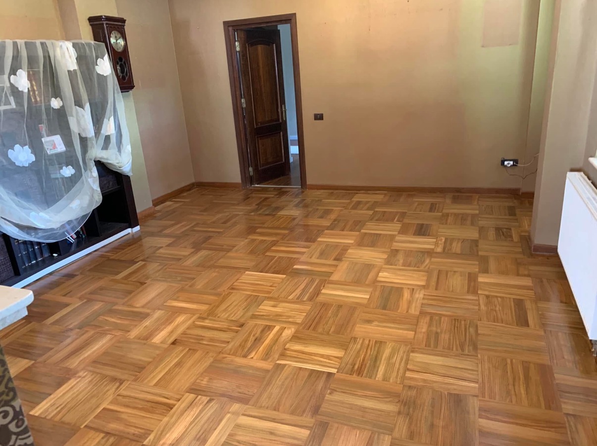 Parkiet ułożony we wzór szachownicy z drewna o ciepłym odcieniu, widok na pokój z otwartymi drzwiami i meblami w tle.