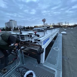 TECHcomplex - Instalator łączy przewody w centrali wentylacyjnej marki Güntner na dachu budynku Selgros Cash&Carry; widoczny zwój kabla, metalowa kratownica i pochmurne niebo.