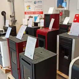 Ekspozycja różnych modeli pieców na pellet w salonie sprzedaży, widoczne etykiety informacyjne i certyfikaty jakości.