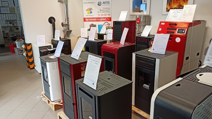 Ekspozycja różnych modeli pieców na pellet w salonie sprzedaży, widoczne etykiety informacyjne i certyfikaty jakości.