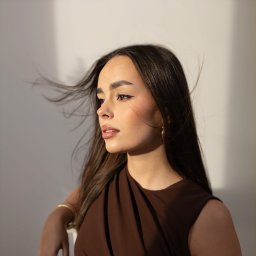 FotoArtist - Portret kobiety z profilu, z delikatnym makijażem, złotymi kolczykami i bransoletką, włosy rozwiane wiatrem, oświetlone naturalnym światłem.