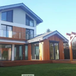 Nowoczesny dom murowany z drewnianą elewacją i tarasem w Warszawie, z widoczną pergolą w ogrodzie.