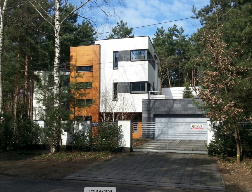 Nowoczesny dom z elewacją w bieli i drewnie, z garażem wykończonym szarym kamieniem, otoczony zielenią i ogrodzeniem z metalowymi przęsłami.