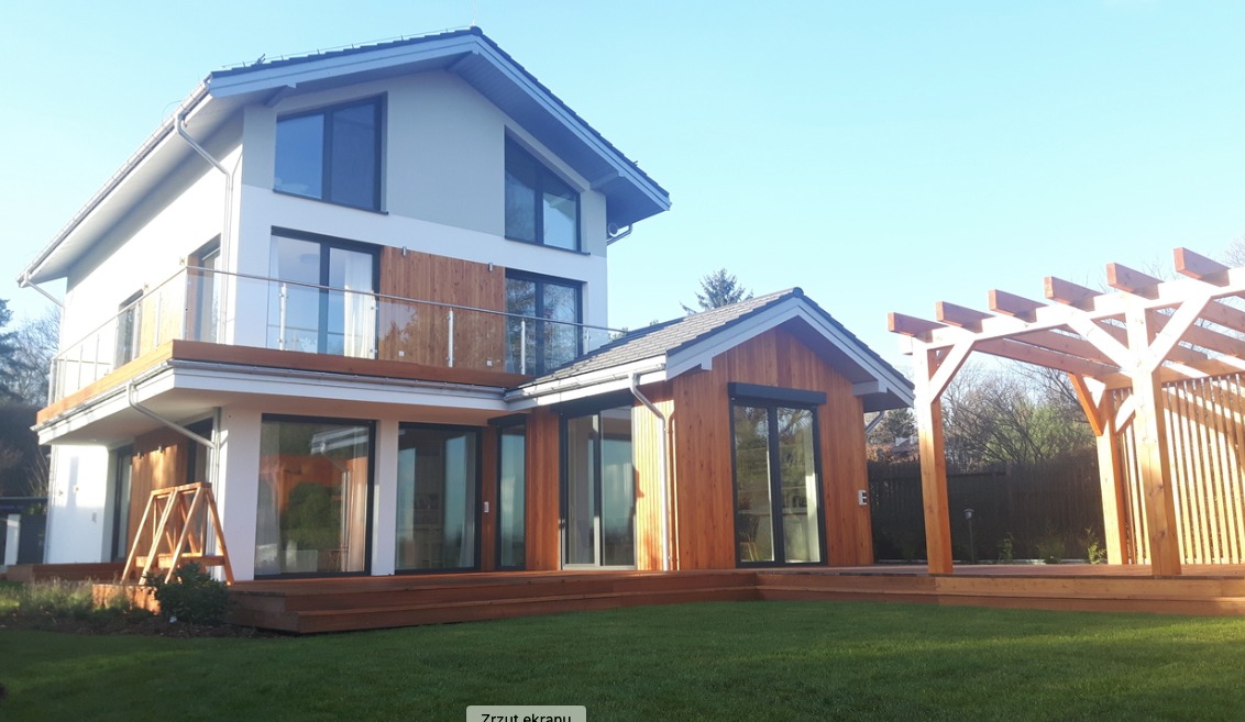 Nowoczesny dom murowany z drewnianą elewacją i tarasem w Warszawie, z widoczną pergolą w ogrodzie.