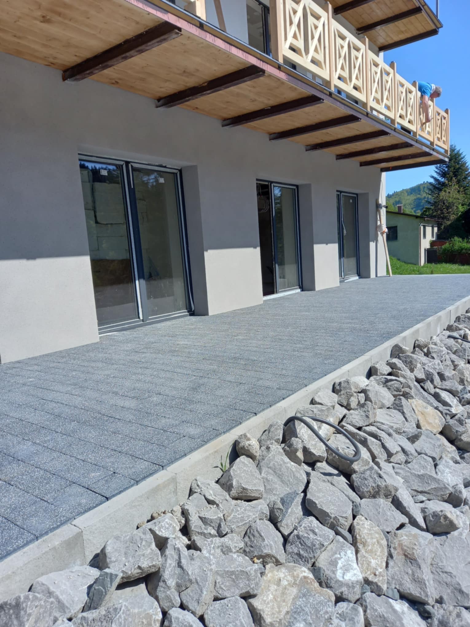 Szara kostka brukowa tworząca chodnik przy nowoczesnym domu z balkonem, zabezpieczona kamieniami po bokach.