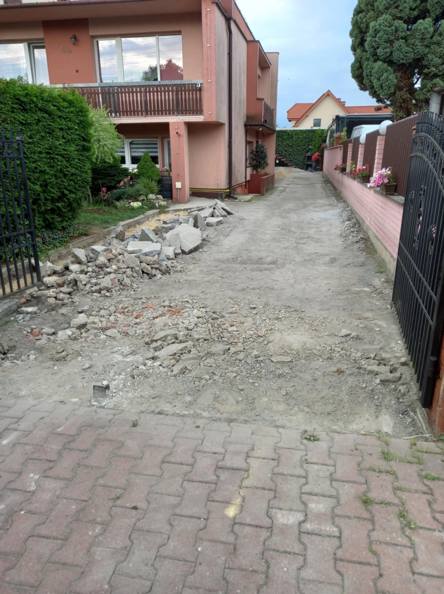 Przygotowanie podłoża pod nową nawierzchnię: rozkruszone stare płyty i gruz na podjeździe przed domem z różową elewacją.
