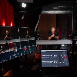 aim-Studio Sp. z o.o. - Studio filmowe: monitor z podglądem z kamer, laptop z oprogramowaniem do montażu, oświetlenie studyjne i osoba w tle, tworząca klimat profesjonalnej produkcji wideo.
