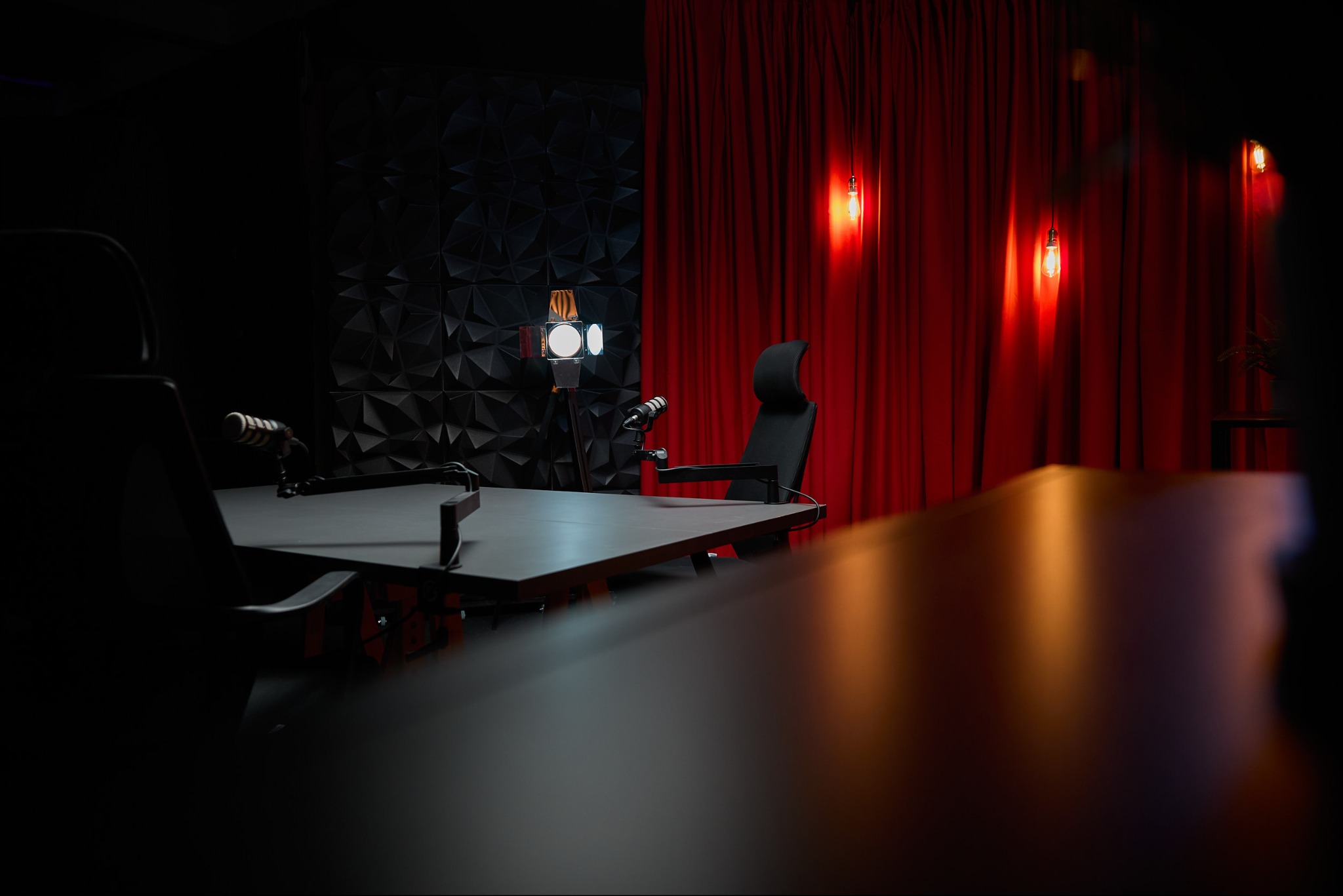 Nowoczesne studio nagrań z mikrofonami, oświetleniem i czerwonymi zasłonami w tle, gotowe do realizacji profesjonalnych nagrań audio i wideo.