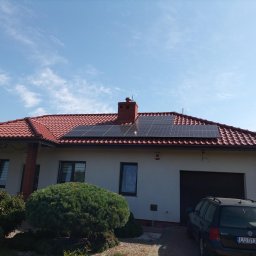 VIAPROFIT SP. Z O.O. SPÓŁKA Z OGRANICZONĄ ODPOWIEDZIALNOŚCIĄ - Instalacja fotowoltaiczna na dachu domu jednorodzinnego z czerwoną dachówką, widok z poziomu ogrodu w słoneczny dzień.