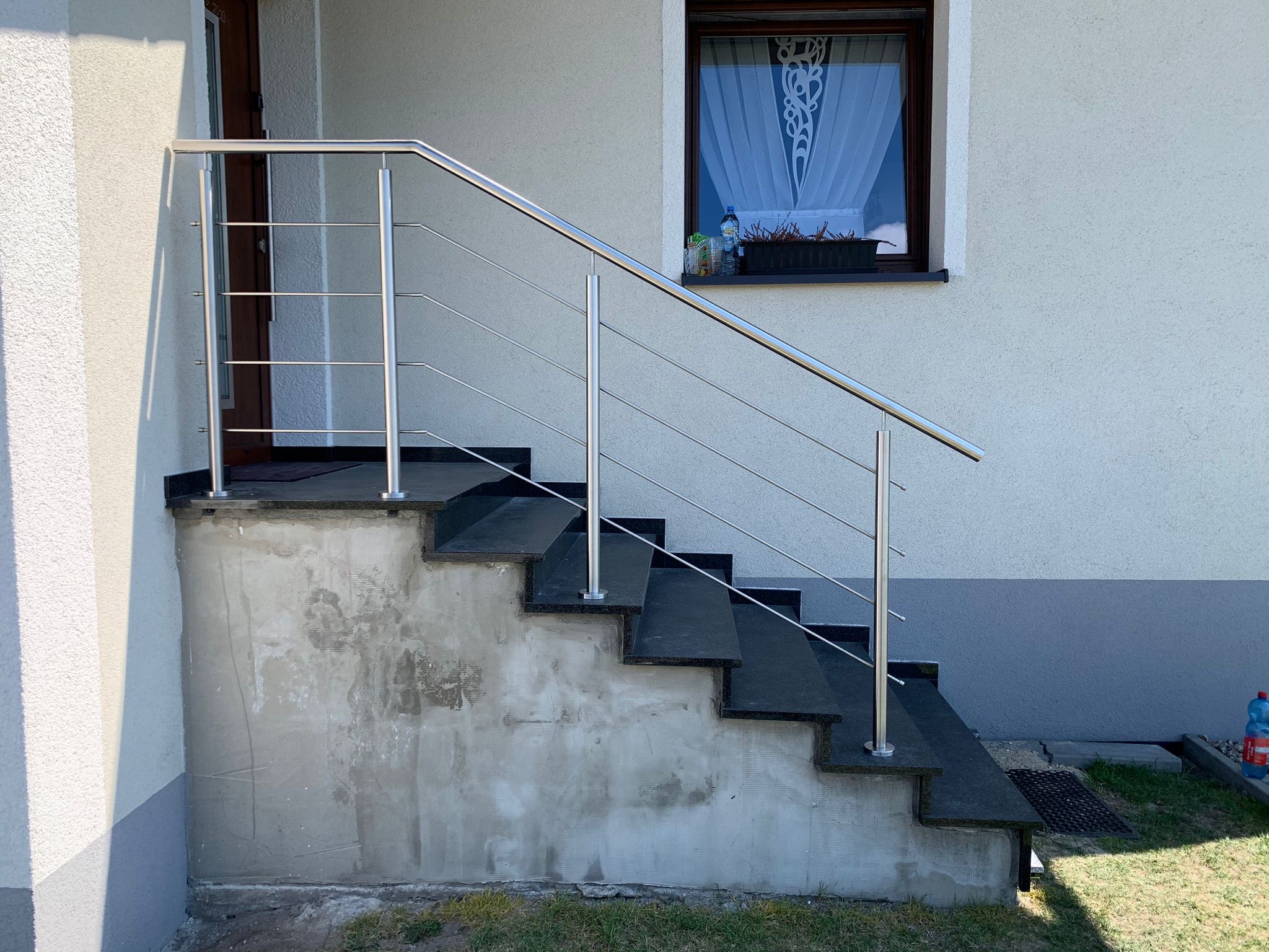 Zewnętrzne schody z czarnego kamienia z metalową poręczą w Katowicach. Widoczne niedoskonałości na ścianie fundamentu.