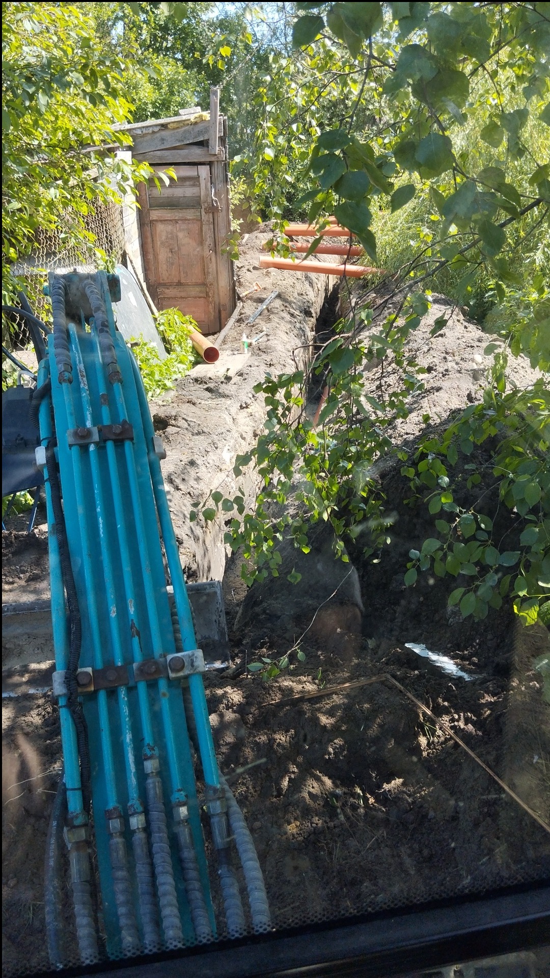 Wykop pod przyłącze wodno-kanalizacyjne w Żukowie, widok z kabiny koparki na wykop z ułożonymi rurami, obok drewniana konstrukcja.