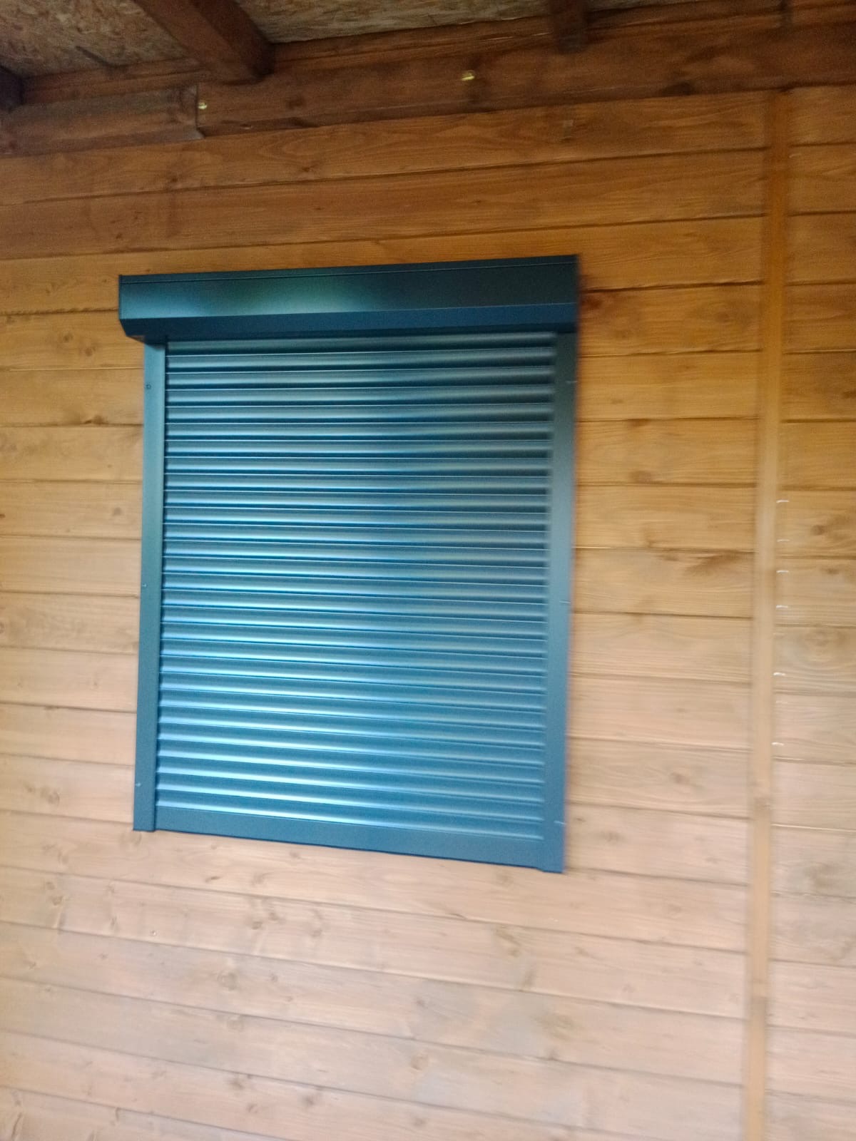 Zamknięta, grafitowa osłona okienna na drewnianej elewacji budynku gospodarczego.