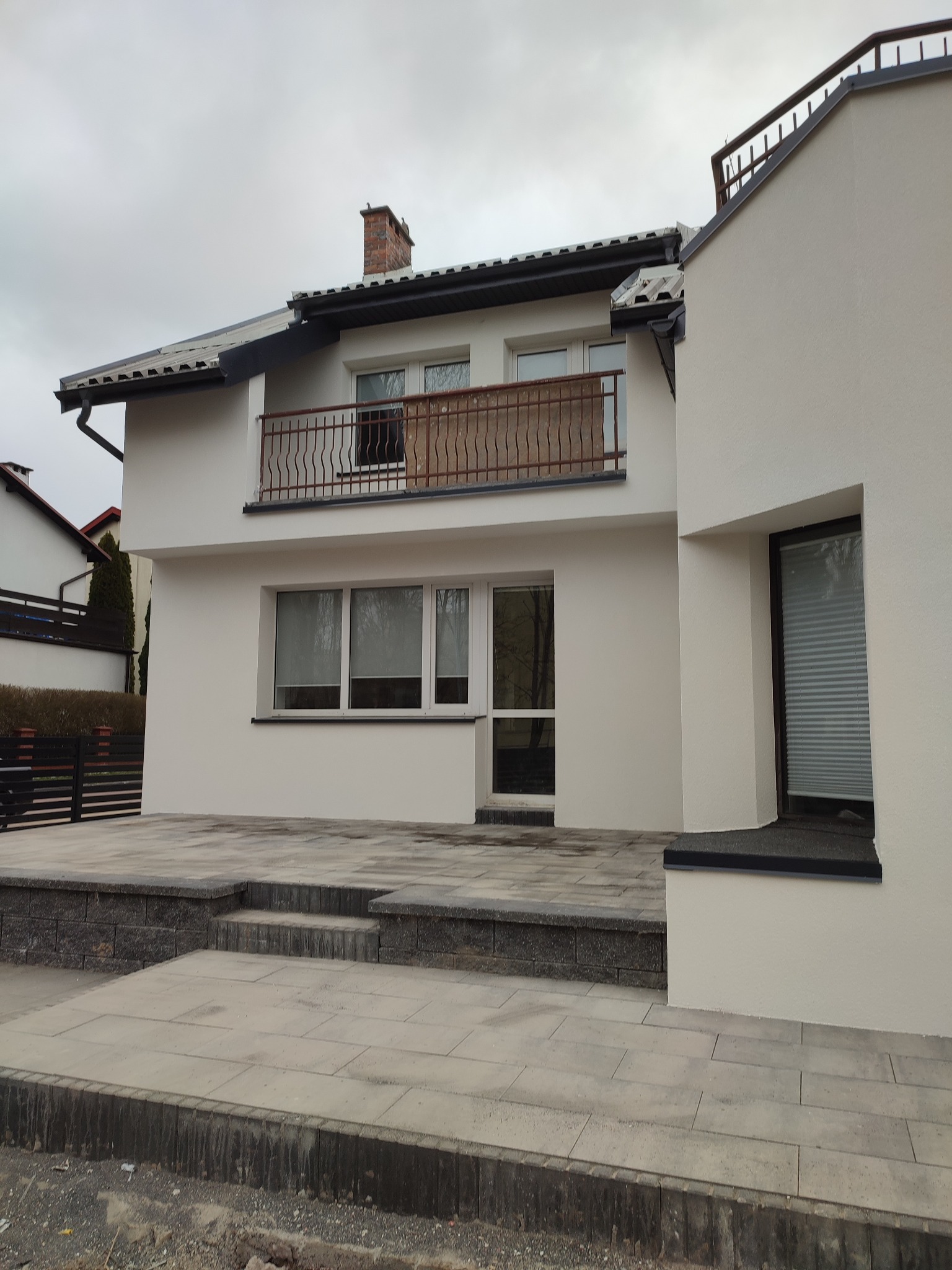 Świeżo otynkowany dom murowany z balkonem i brukowanym tarasem, widok z poziomu gruntu na placu budowy.