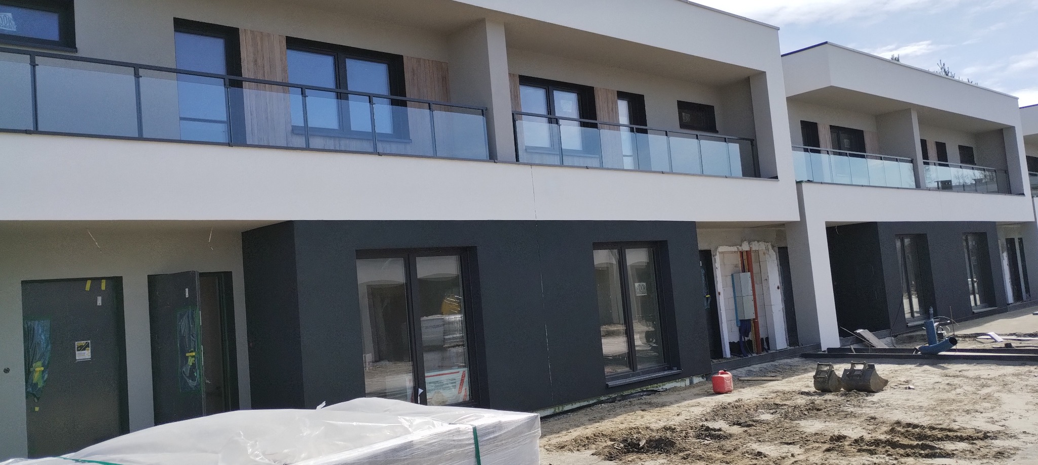 Nowoczesne budynki z balkonami zabezpieczonymi szklanymi balustradami. Ujęcie z dołu, widoczne elementy placu budowy.