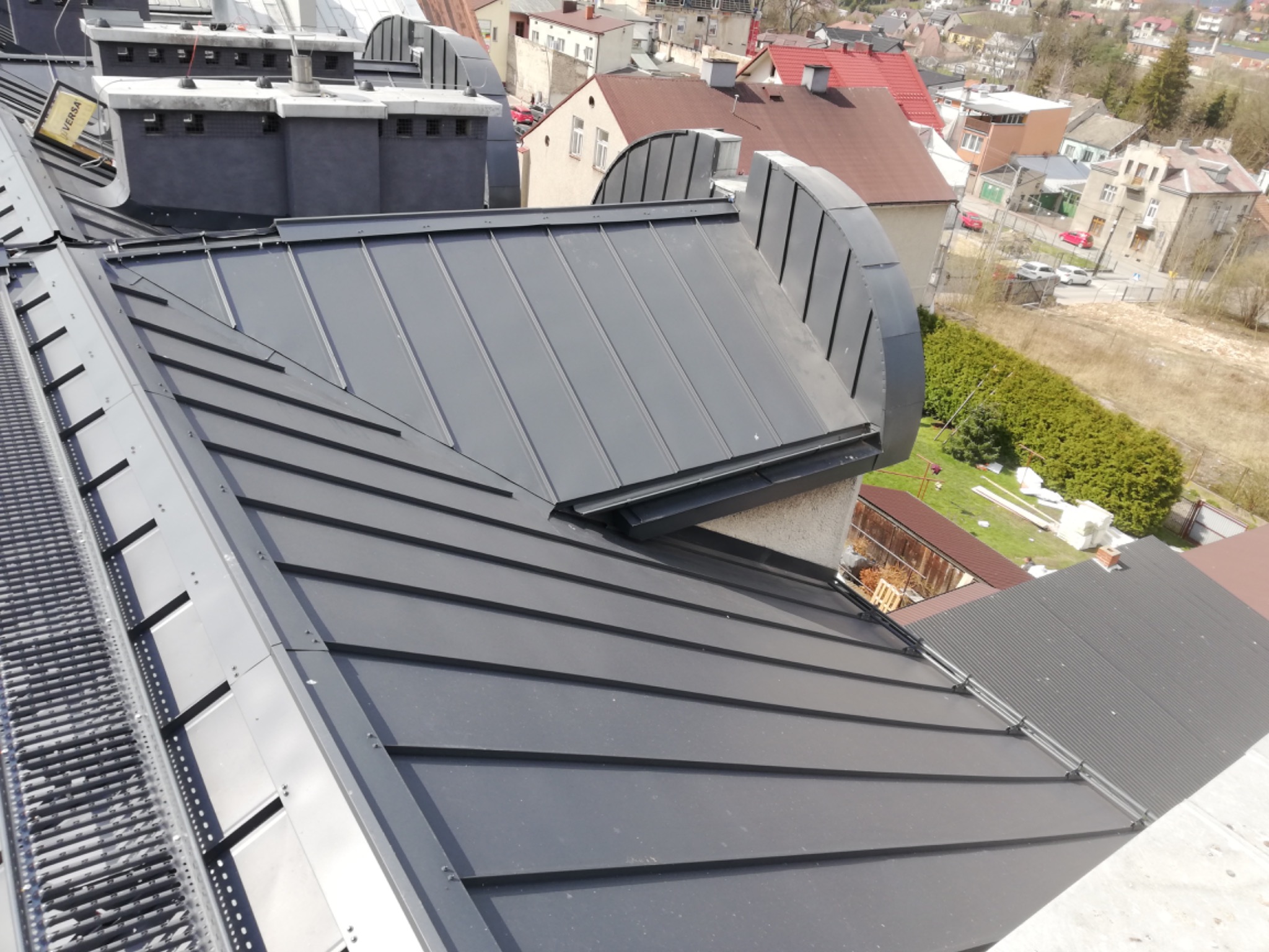 Nowoczesne, grafitowe pokrycie dachowe z blachy na budynku w zabudowie miejskiej, widok z góry, elementy obróbki blacharskiej.