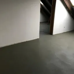 Świeżo wylana, gładka posadzka jastrychowa w jasnym pomieszczeniu na poddaszu z oknami dachowymi i drewnianą konstrukcją więźby.