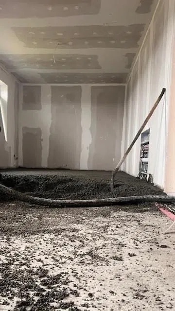 Wylewka jastrychowa w trakcie realizacji w pomieszczeniu z przygotowanymi ścianami, widoczny wąż doprowadzający zaprawę i narzędzie do rozprowadzania masy.