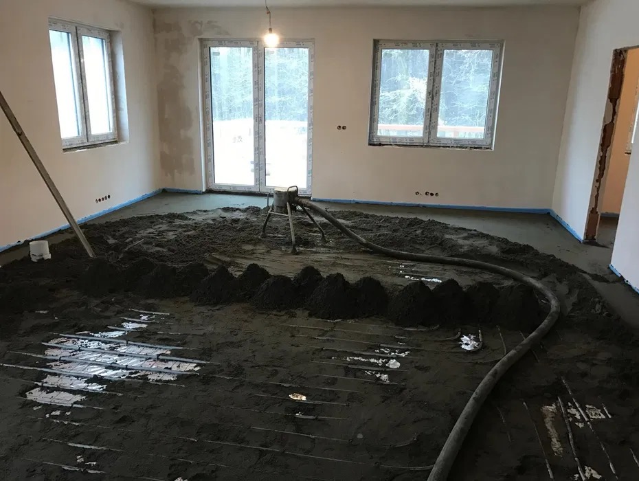 Wylewka jastrychowa w trakcie rozprowadzania na ogrzewanie podłogowe, widoczna maszyna do wylewania i poziomica oparta o ścianę.