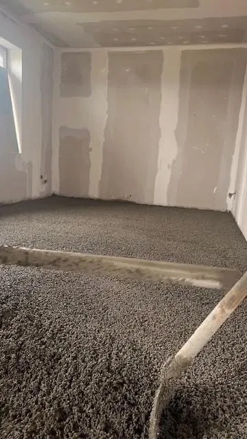 Świeżo wylana, szara posadzka w pomieszczeniu w trakcie remontu, widoczne ślady po narzędziach i niedokończone ściany.