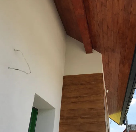 Wykończenie wnętrza: drewniana boazeria na ścianie, biała ściana, drewniany sufit i wystający kabel. Widok z dołu, jasne światło.