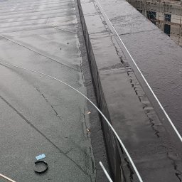 Artur Mroziński - Montaż instalacji odgromowej na dachu budynku w Toruniu, widoczne przewody odprowadzające i elementy mocujące, w tle budynek w trakcie budowy.