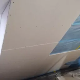 Skośne poddasze z oknem dachowym w trakcie wykańczania, widoczne płyty, izolacja, folia i elementy konstrukcyjne.