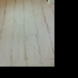 Ułożona podłoga z płytek imitujących drewno, widoczne łączenia i struktura drewna, brązowe drzwi w tle.