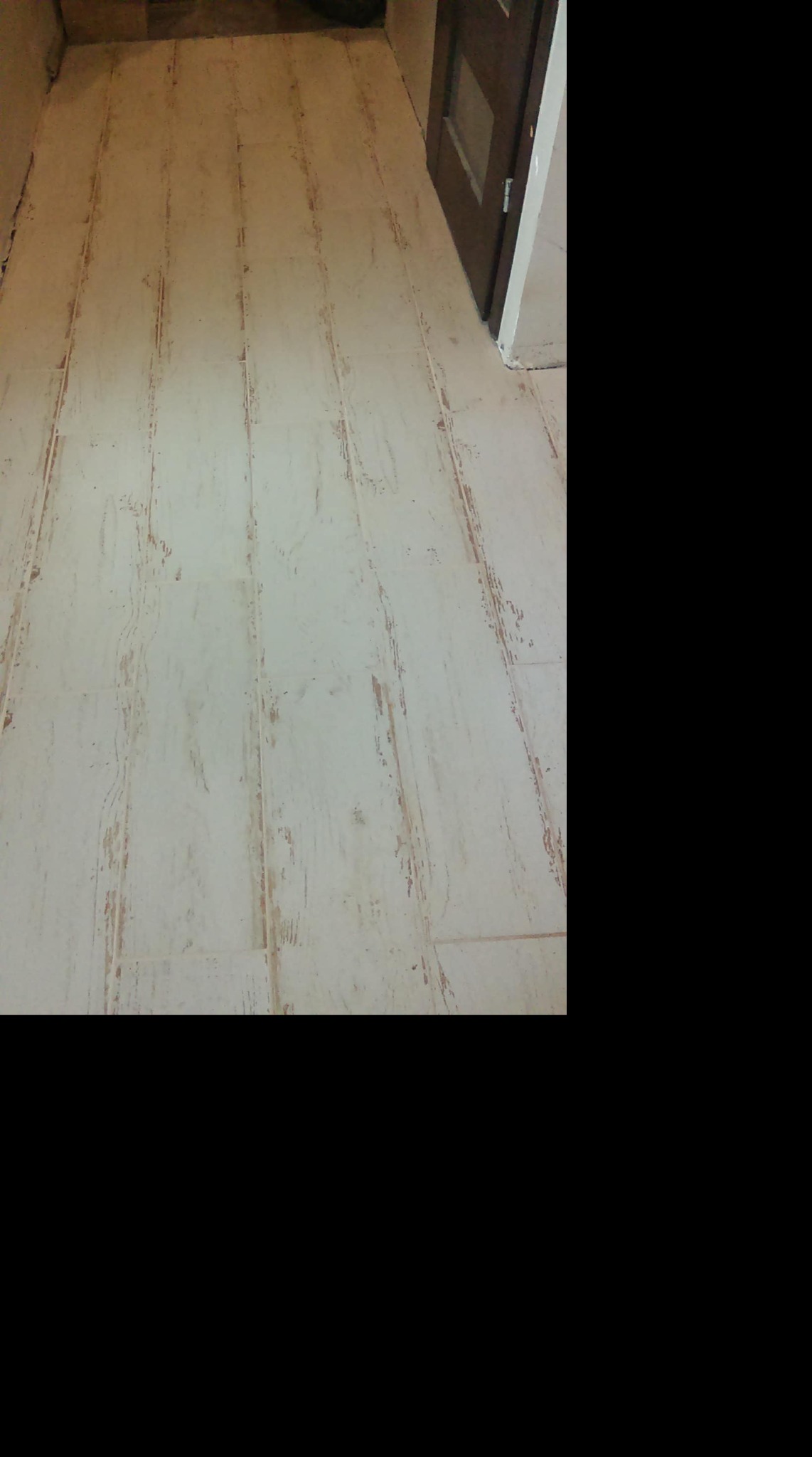 Ułożona podłoga z płytek imitujących drewno, widoczne łączenia i struktura drewna, brązowe drzwi w tle.