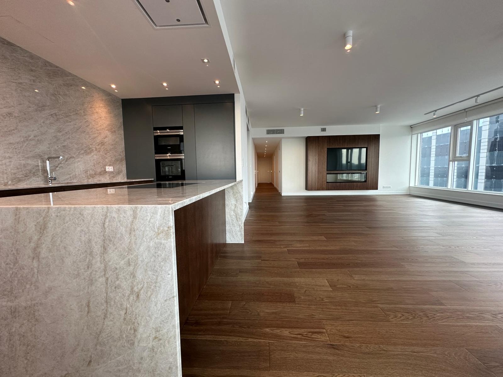 Nowoczesne wnętrze apartamentu z marmurową wyspą kuchenną, parkietem w odcieniach brązu i zabudową kuchenną w kolorze grafitowym, widok z perspektywy niskiego kąta